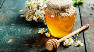 Jar of golden honey with a wooden dipper and flowers – is honey better than sugar?