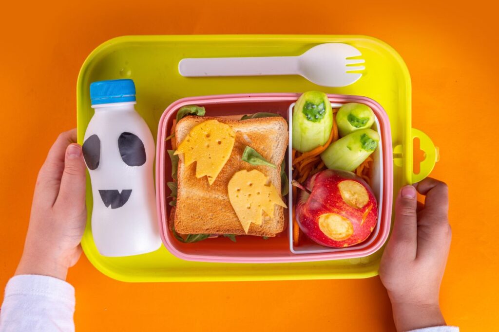 School lunch ideas for kids – child holding a lunchbox with a sandwich, fruit and vegetables