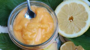 Homemade lemon curd in a glass jar with fresh lemons