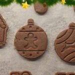 Traditional Polish gingerbread cookies (pierniczki) shaped like Christmas ornaments and a gingerbread house, decorated with festive greenery.