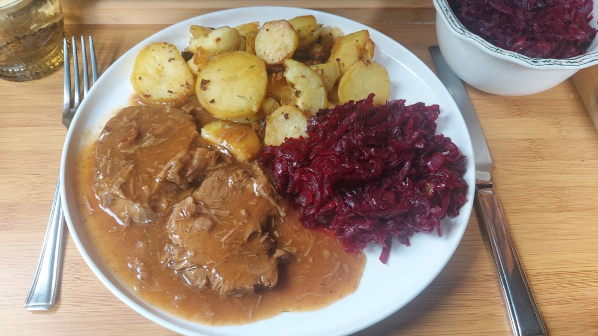 Slow-roasted beef shoulder with rich homemade gravy, golden roasted potatoes and warm Polish beetroot served on a white dinner plate.